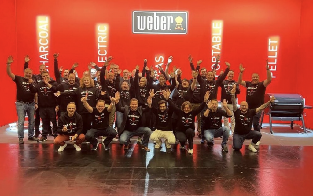 Das Team von Weber auf einer Messe, wo alle gemeinsam die Unternehmenskleidung tragen und sich freuen