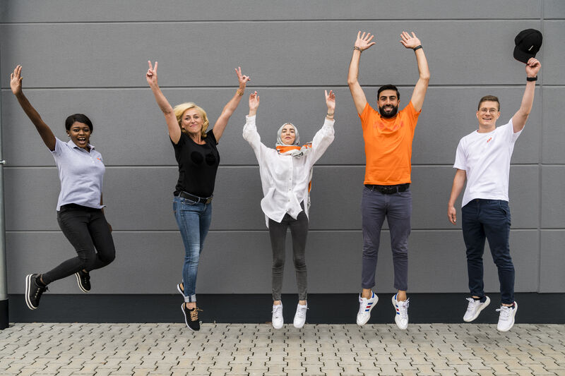 Mitarbeiter eines Facility Dienstleiters im Teamoutfit beim Hüpfen